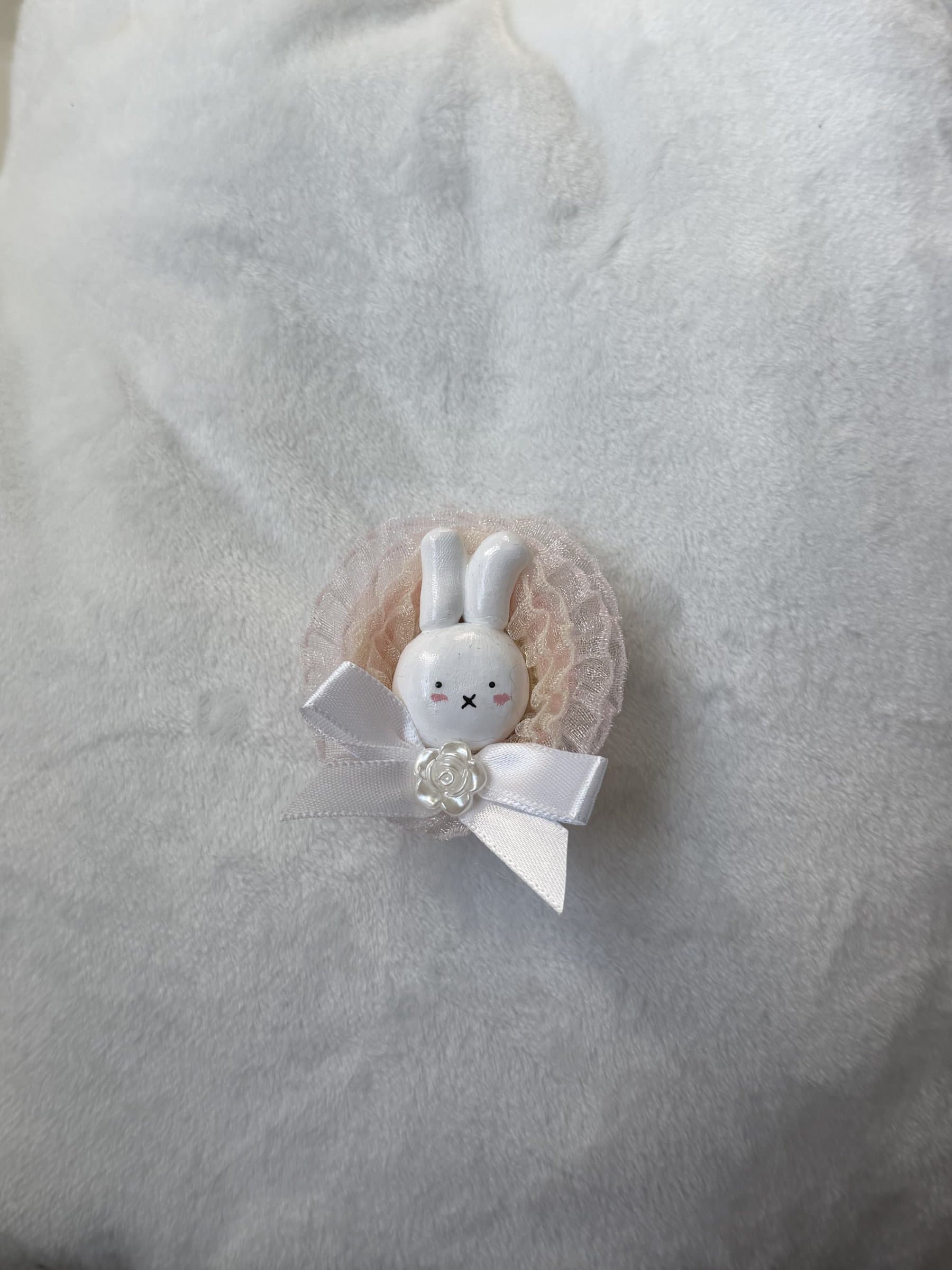 White clay bunny in a peachy pink lace ruffle with a white satin bow and pearl rose, on white plush